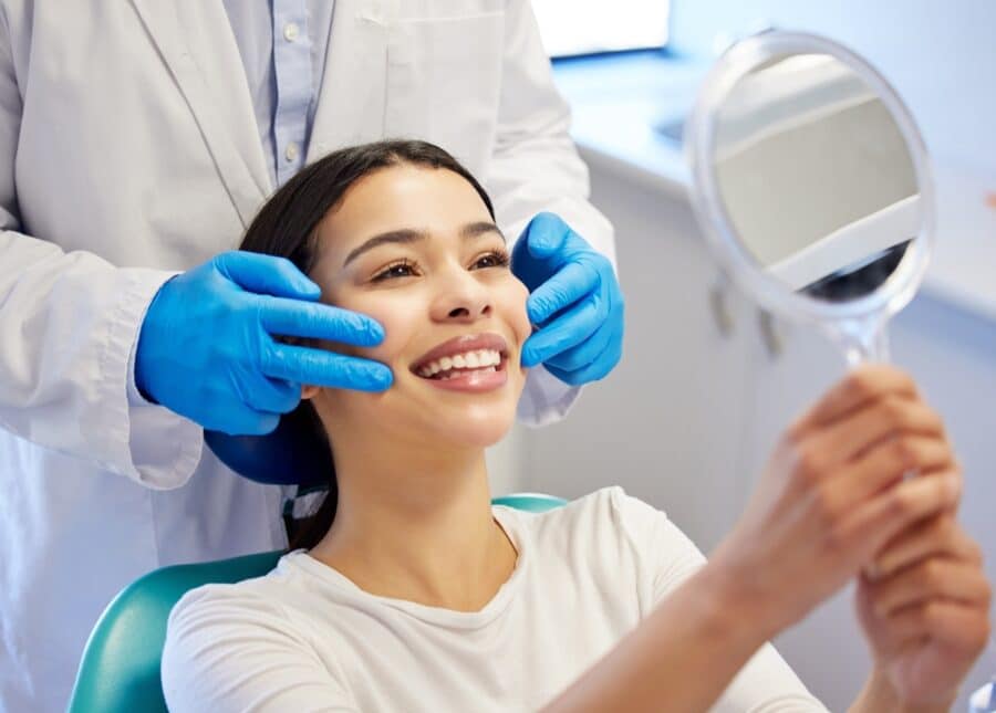 Woman in dentist chair smiling in the mirror at her new dental bridge in Rapid City