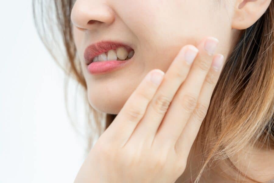 Woman holding her jaw in pain, showing symptoms of toothache from gingivitis, tooth decay, gingival recession, and poor oral hygiene, highlighting the need for dental care, tooth extraction, or treatment for sensitive teeth.
